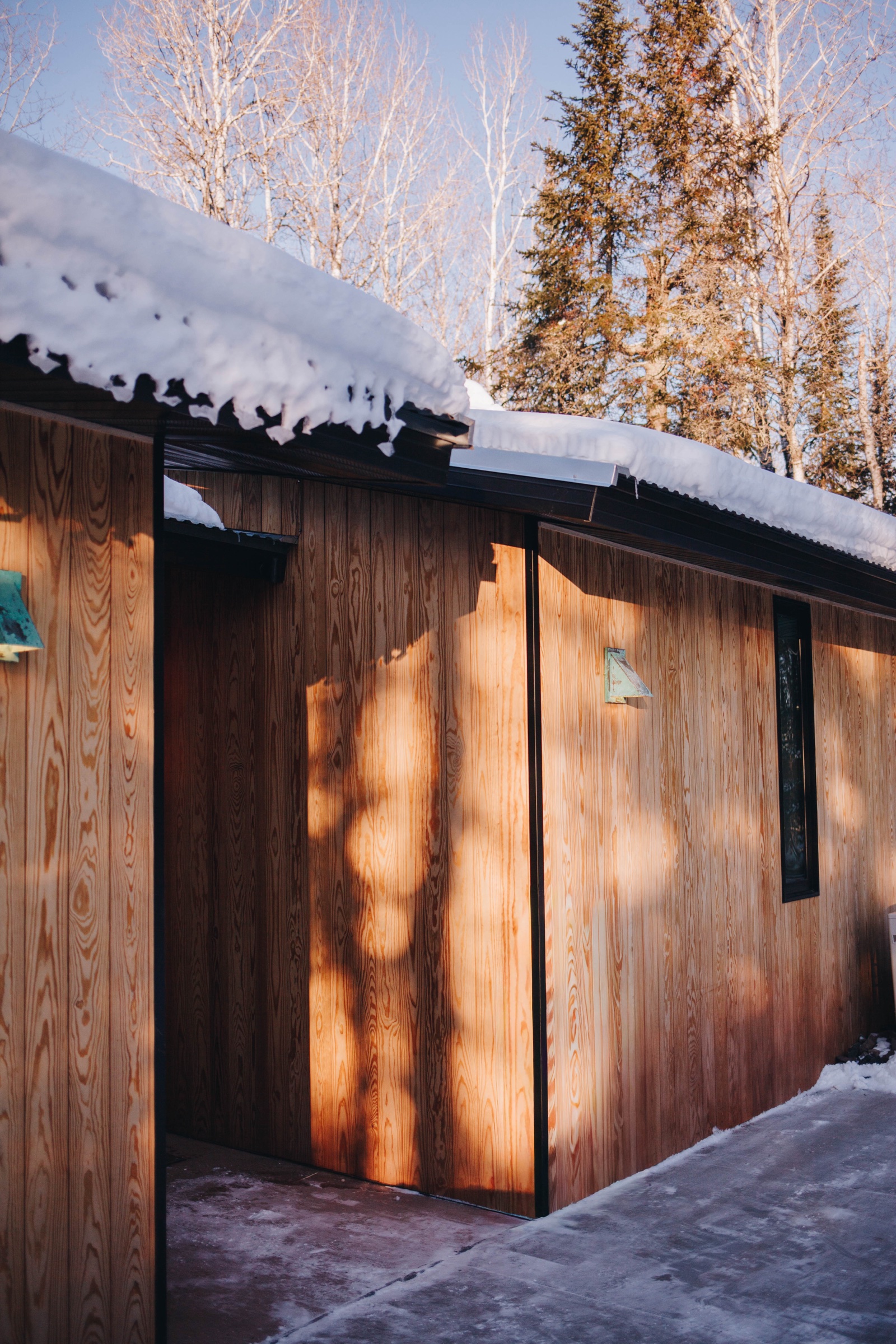 Sentō exterior with golden light on cedar siding and snow on roof