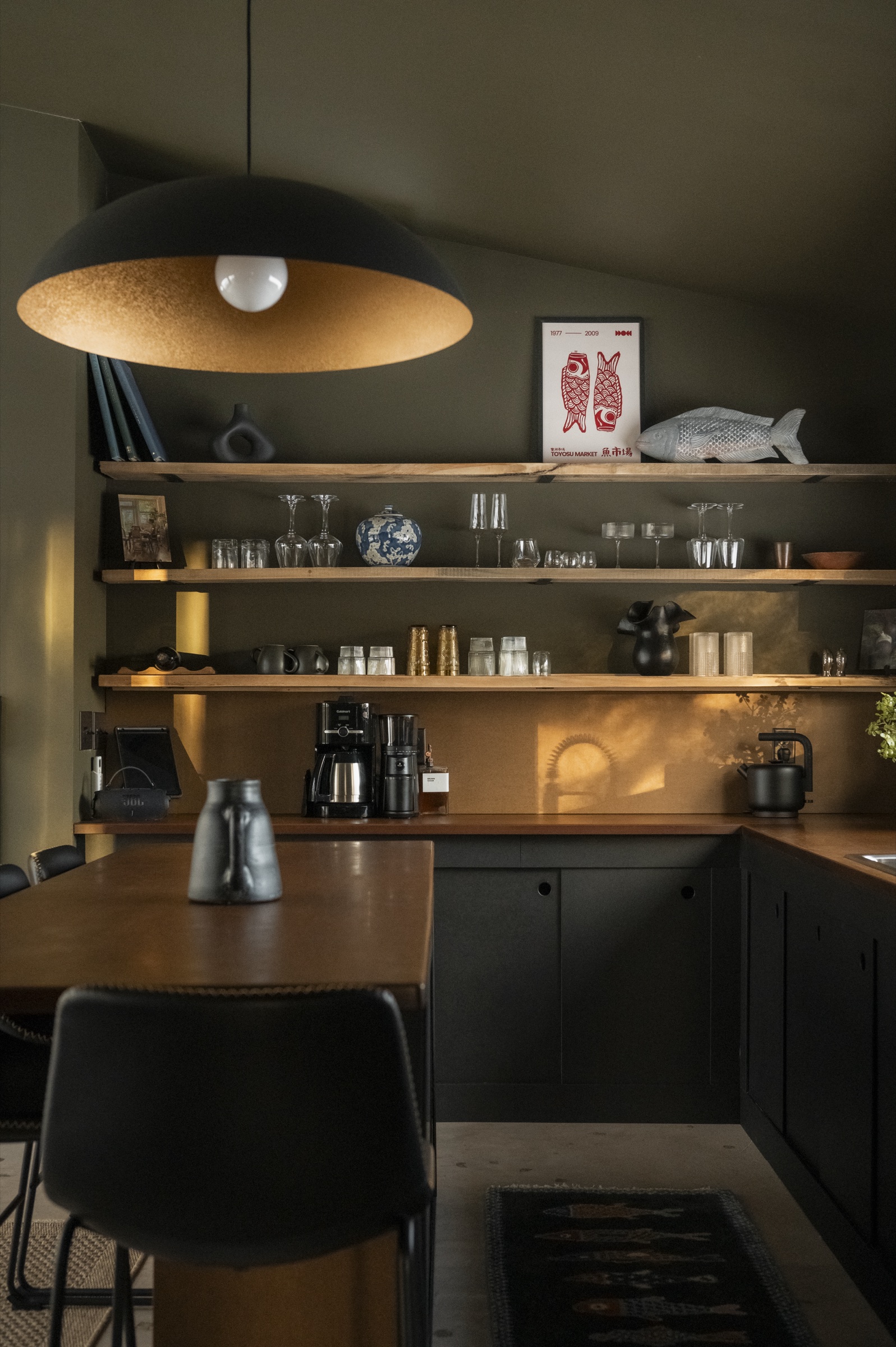 Gourmet kitchen with dark cabinetry, open wood shelving, and dome pendant light