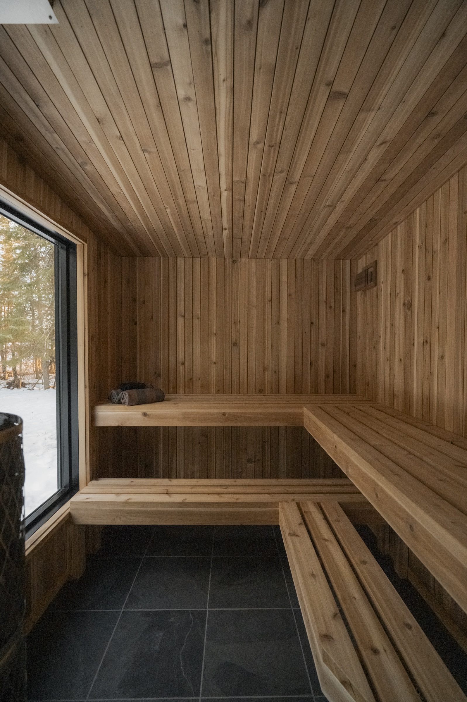 IKI cedar sauna interior with tiered benches and window looking out at snow