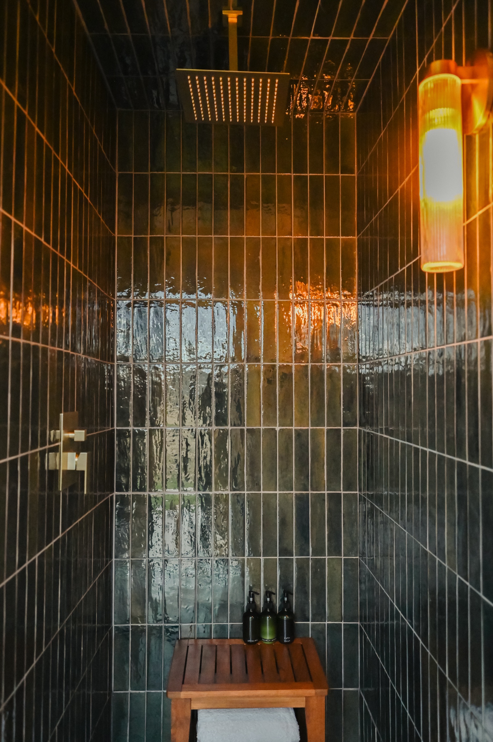 Rain shower head with moody dark tile and pendant lighting